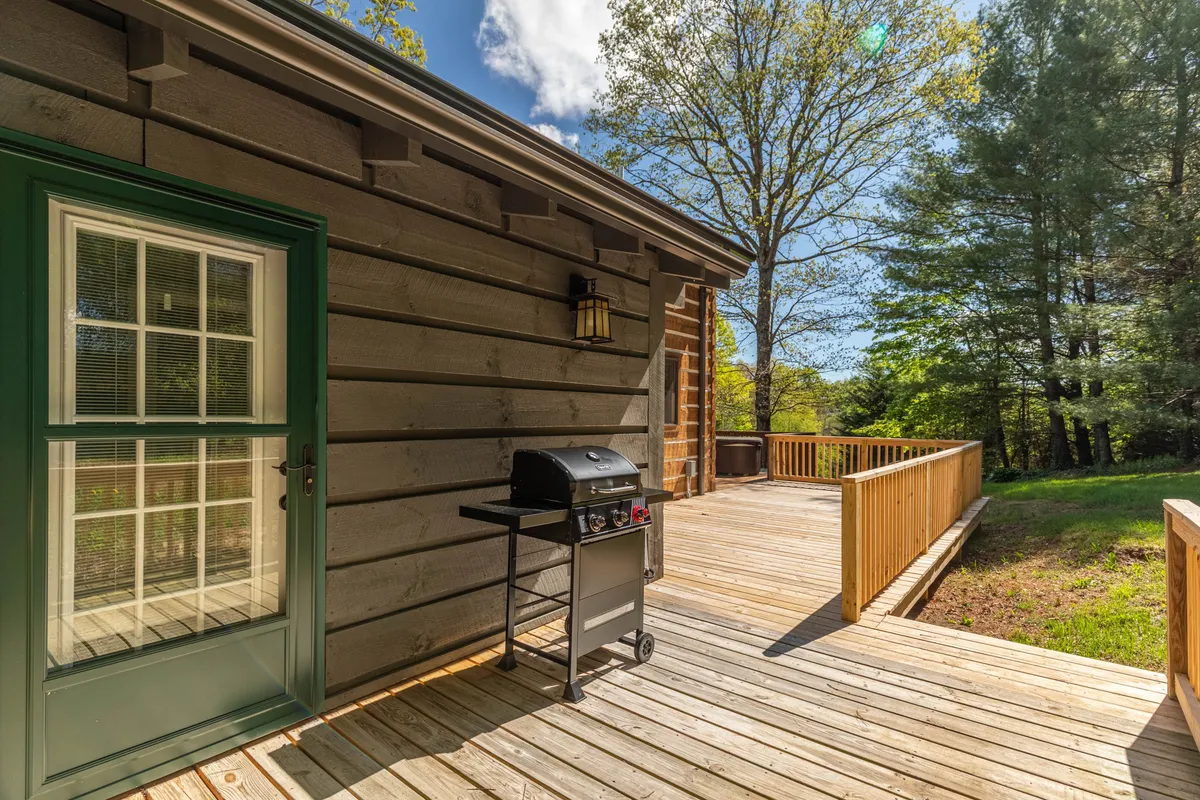 An exterior shot of the wooden deck featuring a grill, surrounded by lush mountain greenery. The space is designed for outdoor dining and barbecues, with comfortable seating and a welcoming atmosphere just steps from the kitchen.