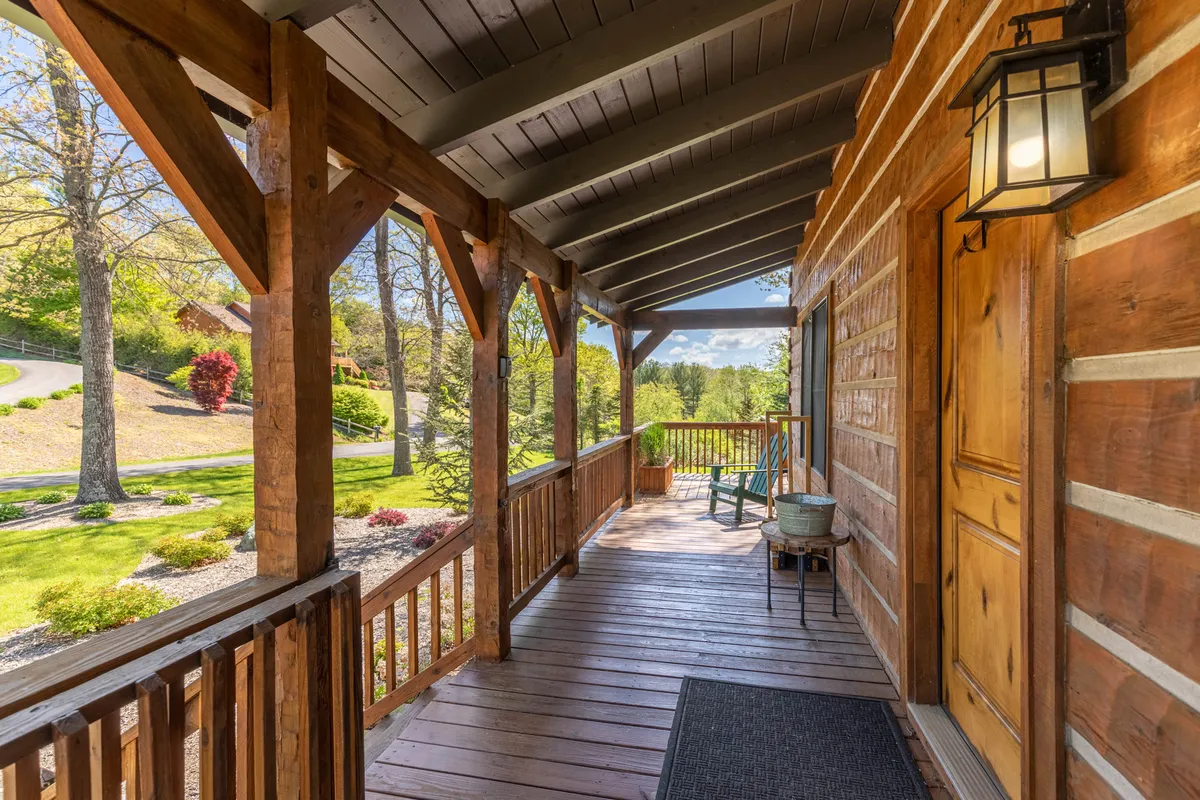 A welcoming wooden porch with a rocking chair and landscaped garden greets visitors at the cabin's entrance. Morning sunlight filters through the trees, creating an inviting space to unwind, socialize, or simply enjoy the views before or after a day out.