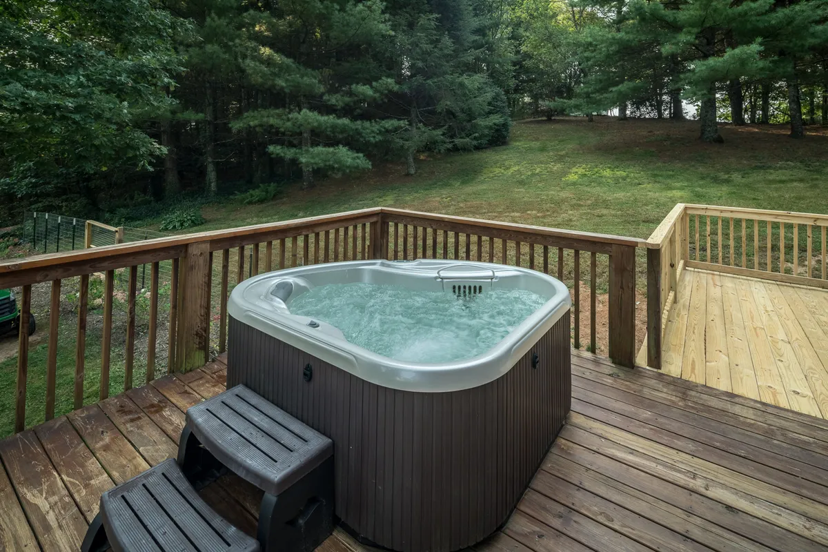 A wooden deck featuring a two-seater hot tub, set against a backdrop of towering trees. The tranquil scene invites relaxation after a day of mountain adventures, with opportunities for stargazing or enjoying coffee outside. The private outdoor space offers a seamless blend of comfort and nature.